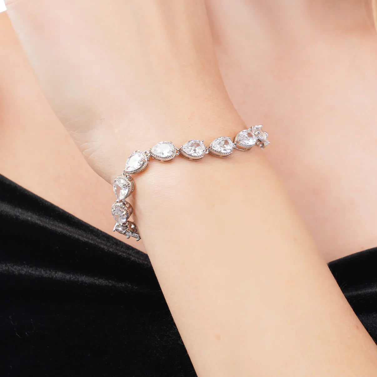 Silver bracelet with clear stones on a person's wrist against a black background