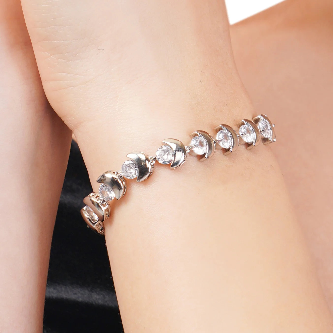 Silver bracelet with clear stones on a person's wrist against a neutral background