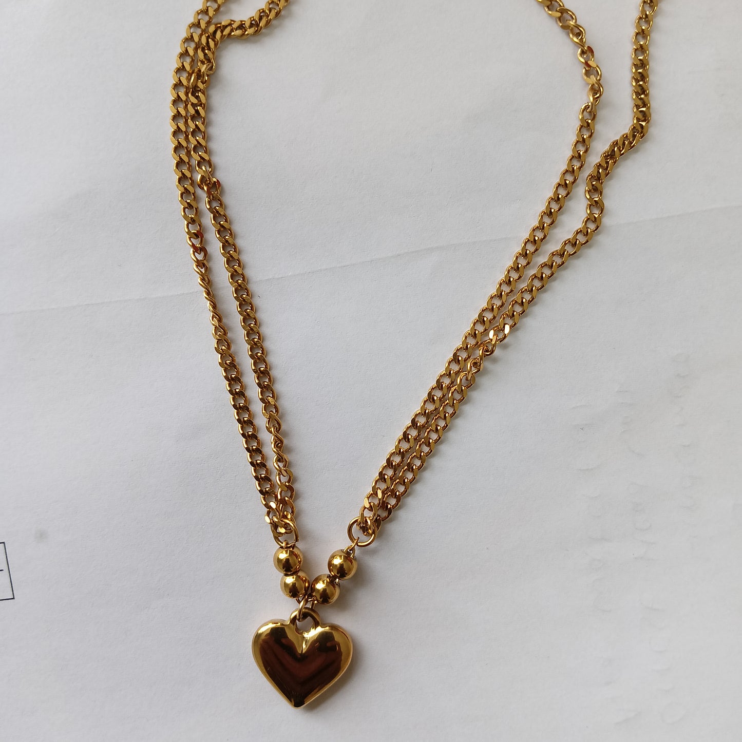 Gold chain necklace with a heart-shaped pendant on a white background