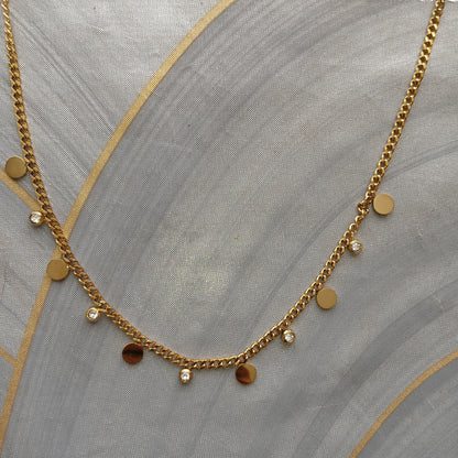 Gold chain necklace with round pendants on a gray fabric background