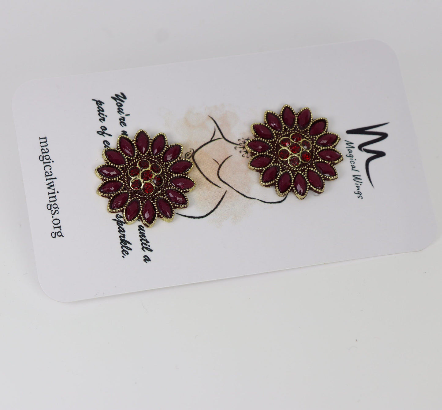 A pair of maroon colored floral wine stud earrings displayed on a white card with the brand 'Magical Wings' written on it.