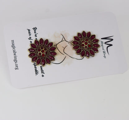 A pair of maroon colored floral wine stud earrings displayed on a white card with the brand 'Magical Wings' written on it.