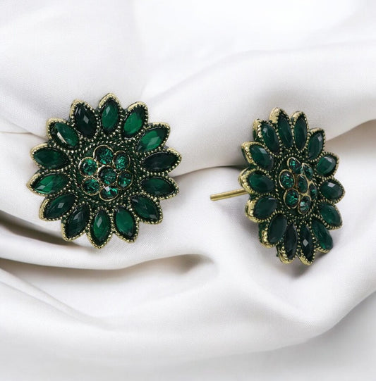 A pair of dark green floral patterned stud earrings on a white fabric surface.