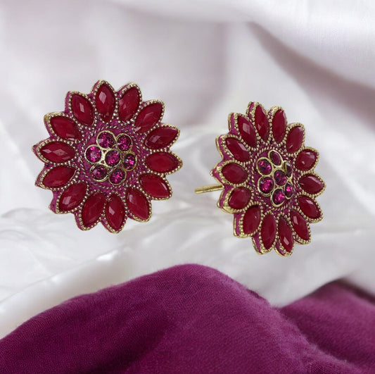 A pair of magenta kundan earrings with gold embellishments on a white and purple fabric surface.