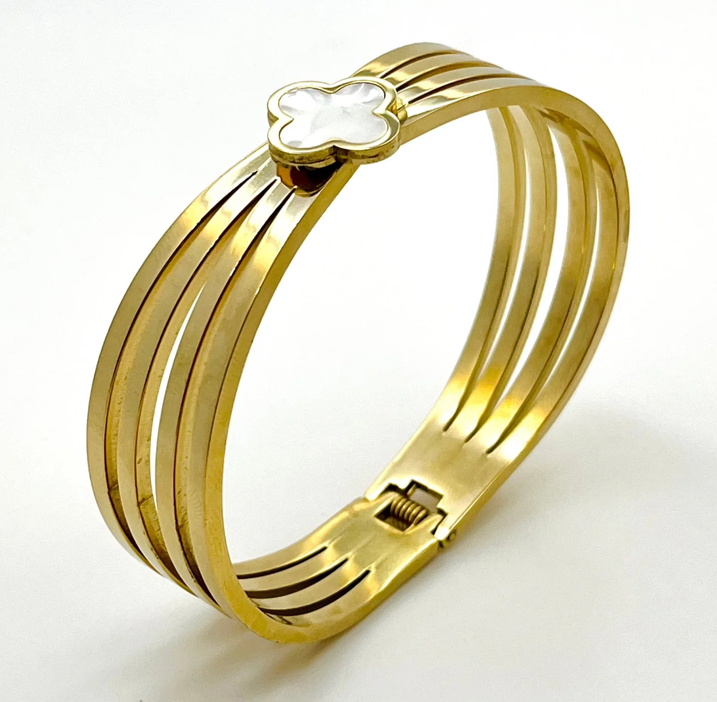 A gold-colored bangle bracelet with a clover design at the clasp.