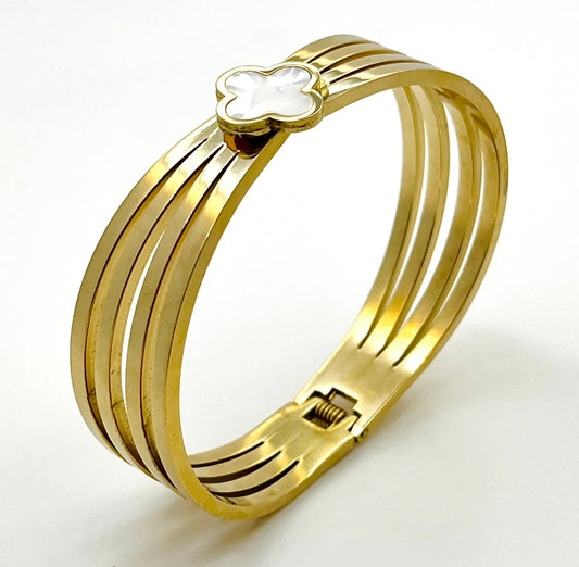A gold-colored bangle bracelet with a clover design at the clasp.