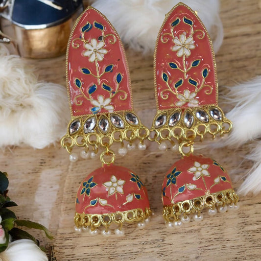 A pair of peach-colored Meenakari earrings with floral patterns and pearl accents, displayed against a fabric background.