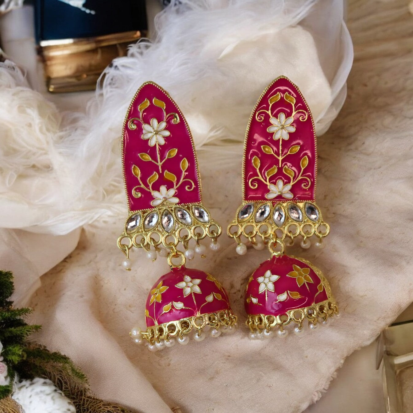 A pair of Meenakari earrings with a gold and magenta design, adorned with small white flowers and pearls.
