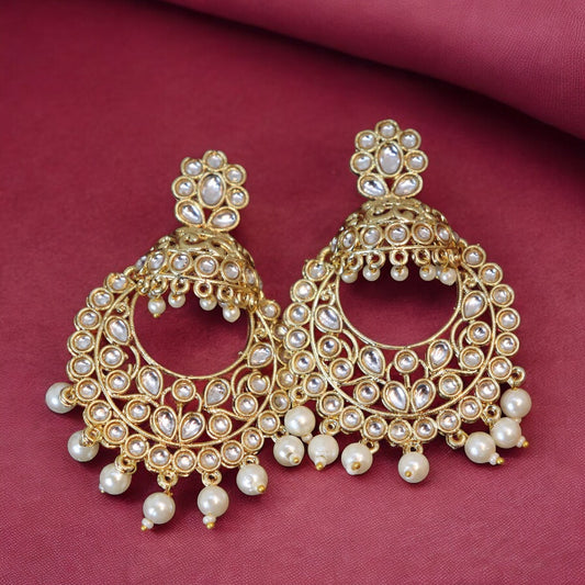 A pair of golden kundan chandbali earrings with pearl embellishments on a pink background.