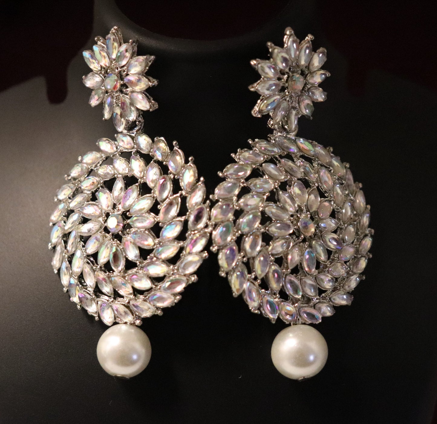 A pair of silver Chandbali earrings featuring a intricate pattern of rainbow crystals and pearl drops.