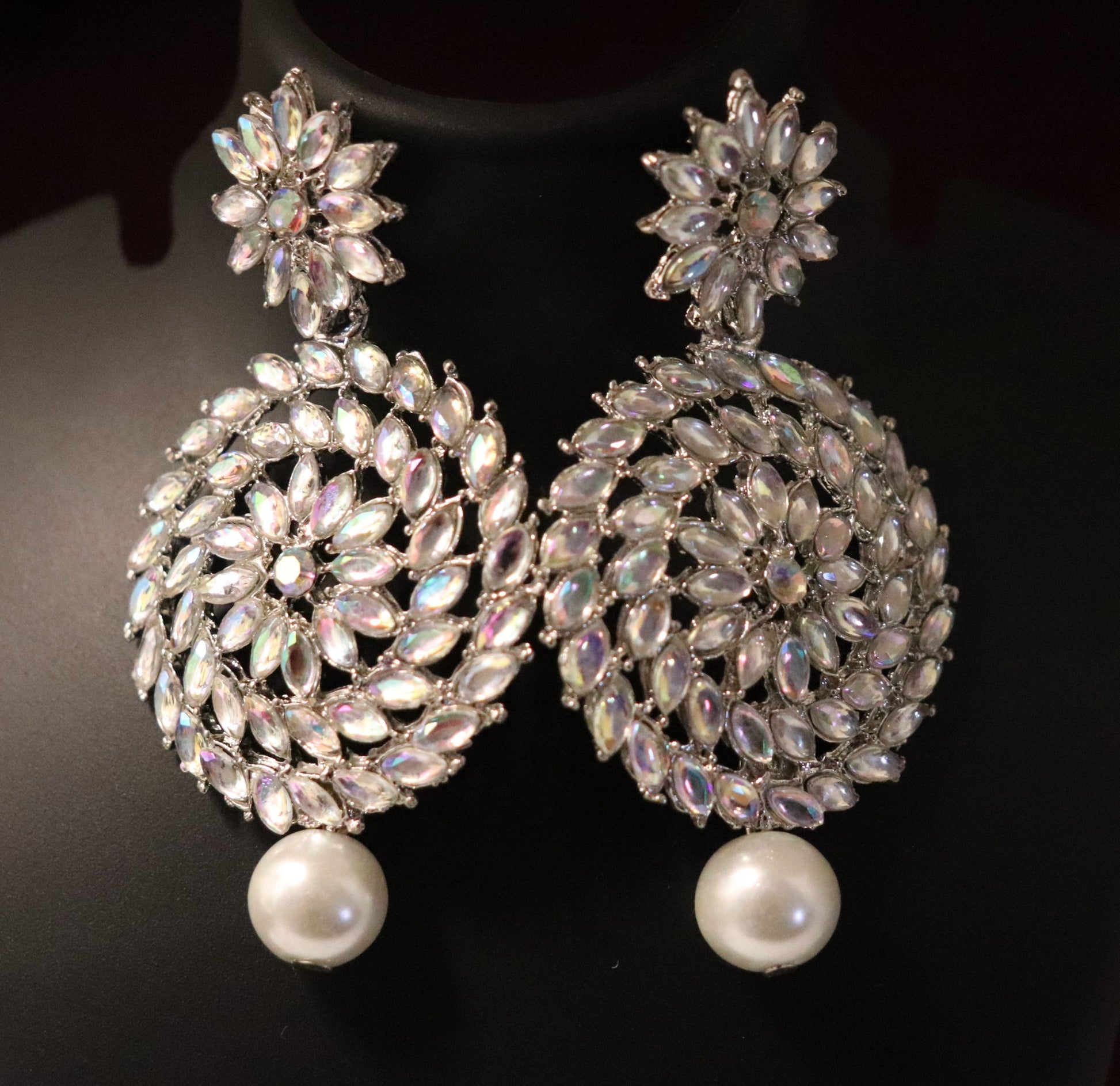 A pair of silver Chandbali earrings featuring a intricate pattern of rainbow crystals and pearl drops.