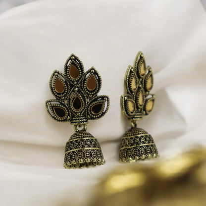 A pair of golden jhumki earrings with intricate leaf patterns, displayed on a white fabric surface.