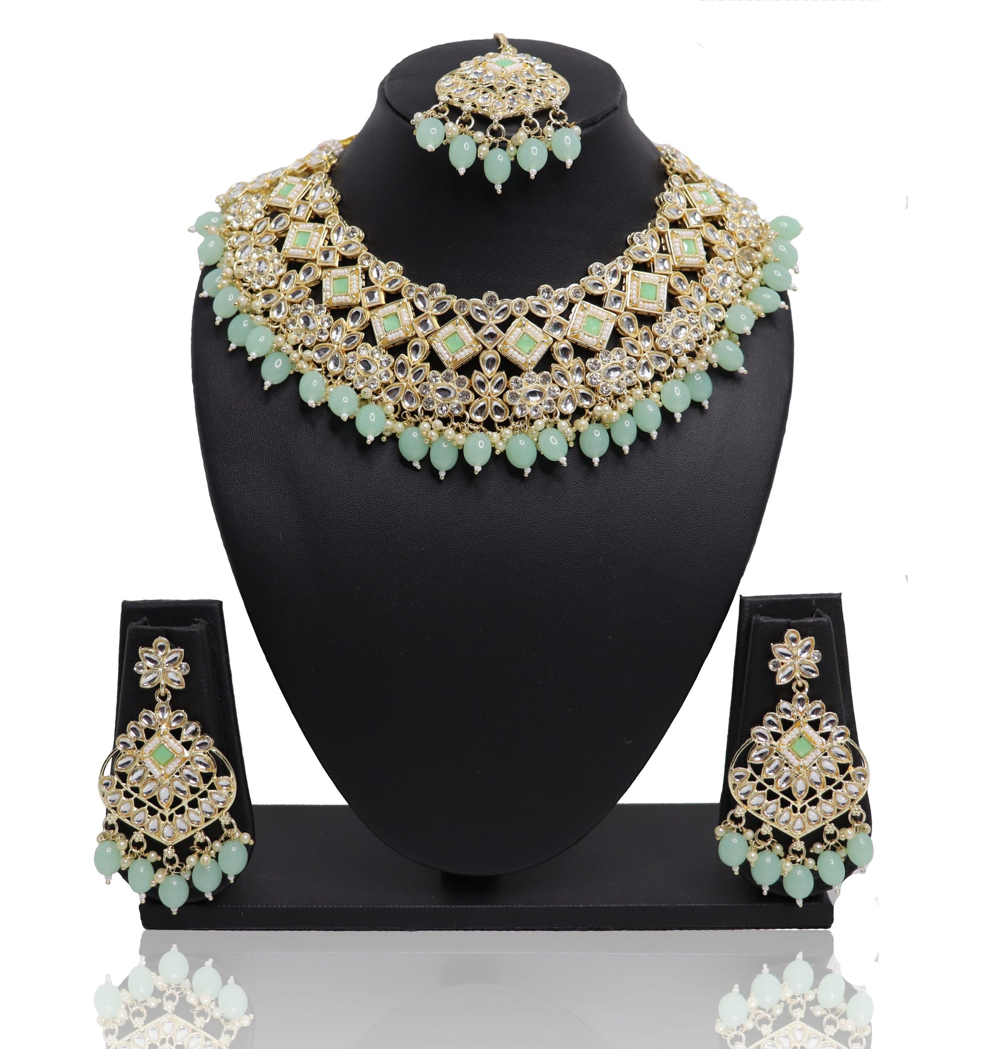 A necklace set with green and gold colors displayed on a mannequin bust, including a necklace, earrings, and a mangtikka.