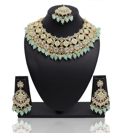 A necklace set with green and gold colors displayed on a mannequin bust, including a necklace, earrings, and a mangtikka.