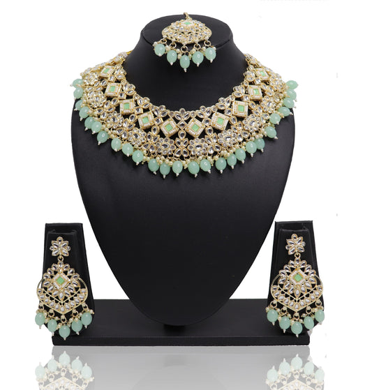 A necklace set with green and gold colors displayed on a mannequin bust, including a necklace, earrings, and a mangtikka.