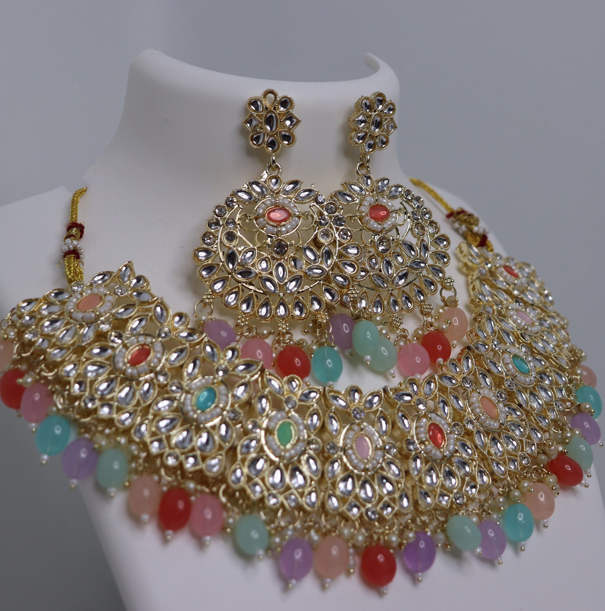 A mannequin showcasing a multi-colored bridal necklace set with intricate gold detailing and bead embellishments.
