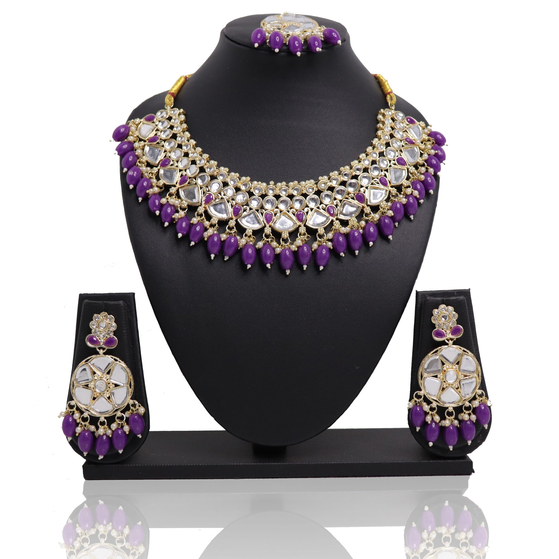 A violet bead mirror necklace set with a mangtikka and earrings displayed on a black stand.