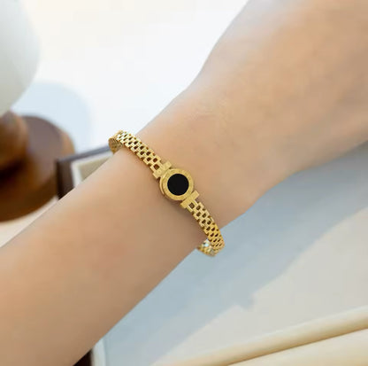 A 18K gold bangle bracelet with a zigzag pattern worn on a person's wrist.