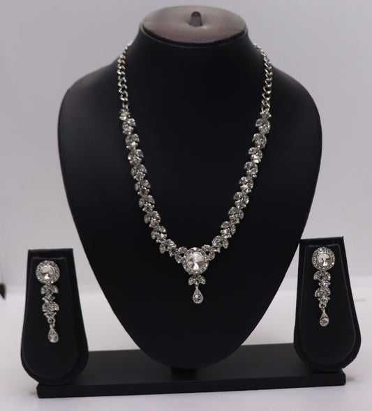 A silver necklace and earrings set displayed on a black mannequin with a prominent central stone and intricate designs.