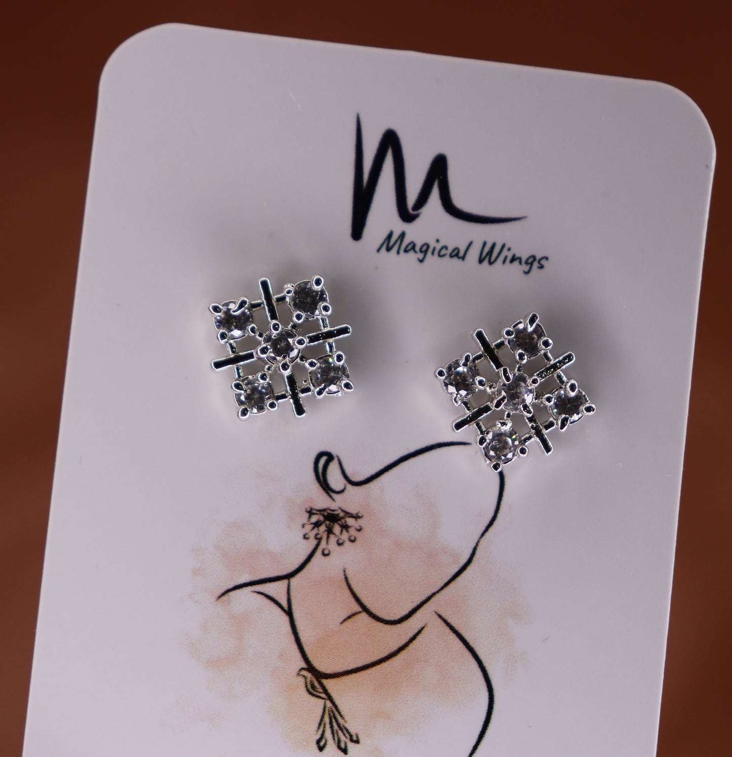 A pair of stud earrings with a geometric pattern, displayed on a branded card with 'Magical Wings' logo.