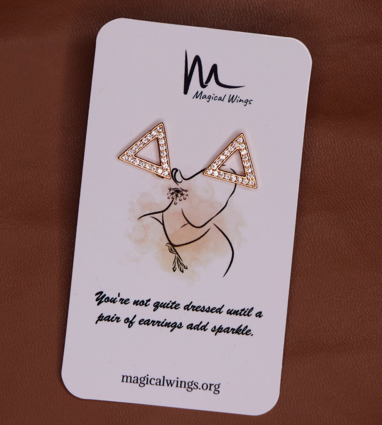 A pair of stud earrings with a geometric triangular design, featuring text on a card that reads 'Magical Wings' and a quote about earrings adding sparkle.