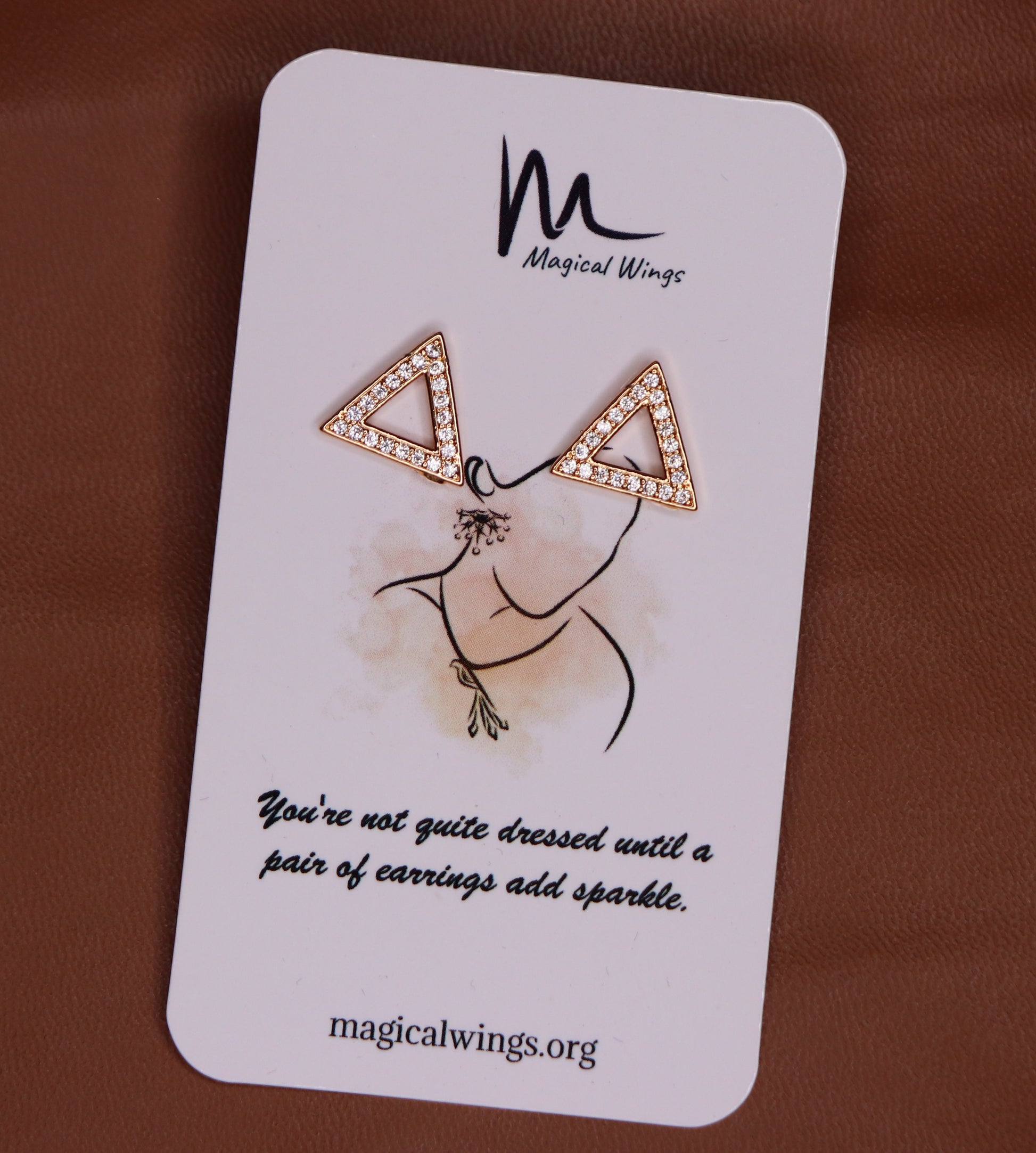 A pair of stud earrings with a geometric triangular design, featuring text on a card that reads 'Magical Wings' and a quote about earrings adding sparkle.