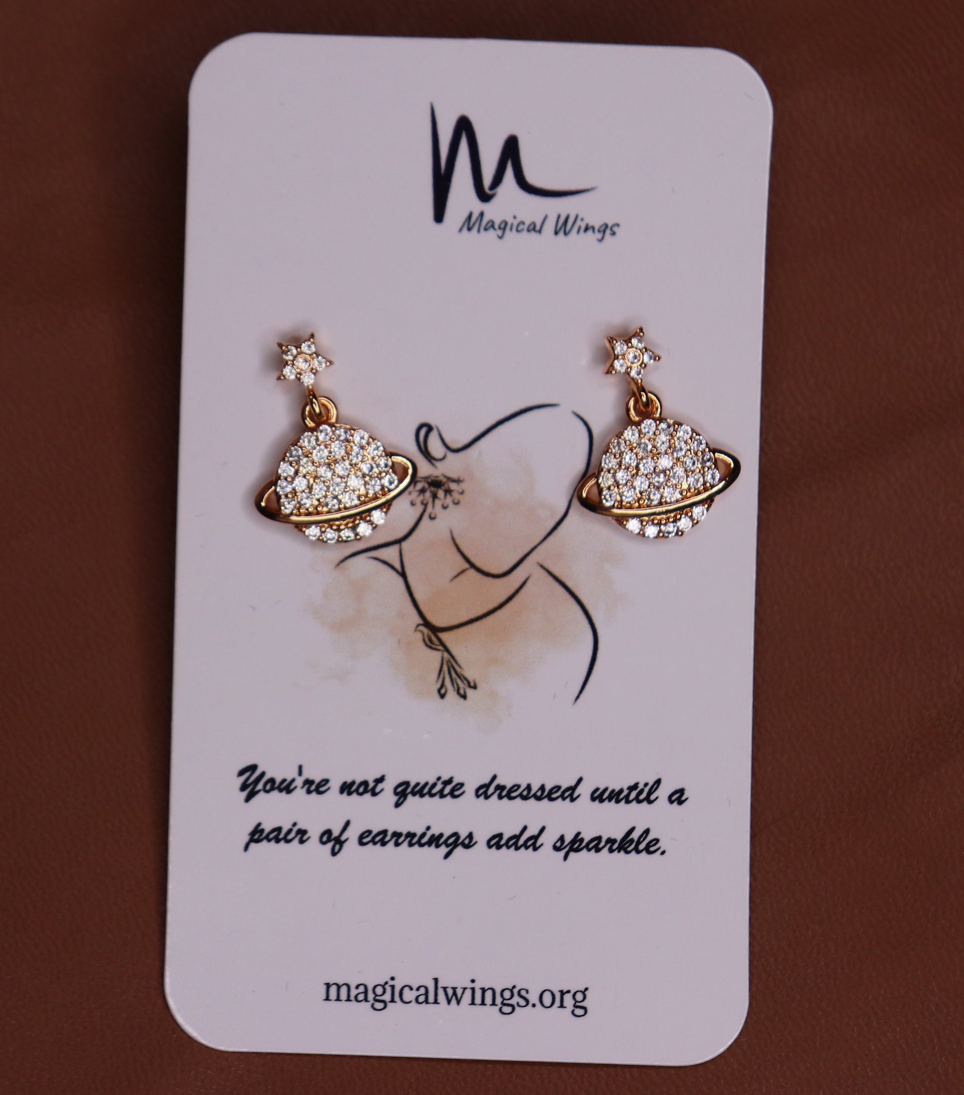 A pair of AD (acrylic) earrings on a card with the Magical Wings logo, featuring a gold-tone stud with a floral design and clear acrylic embellishments.