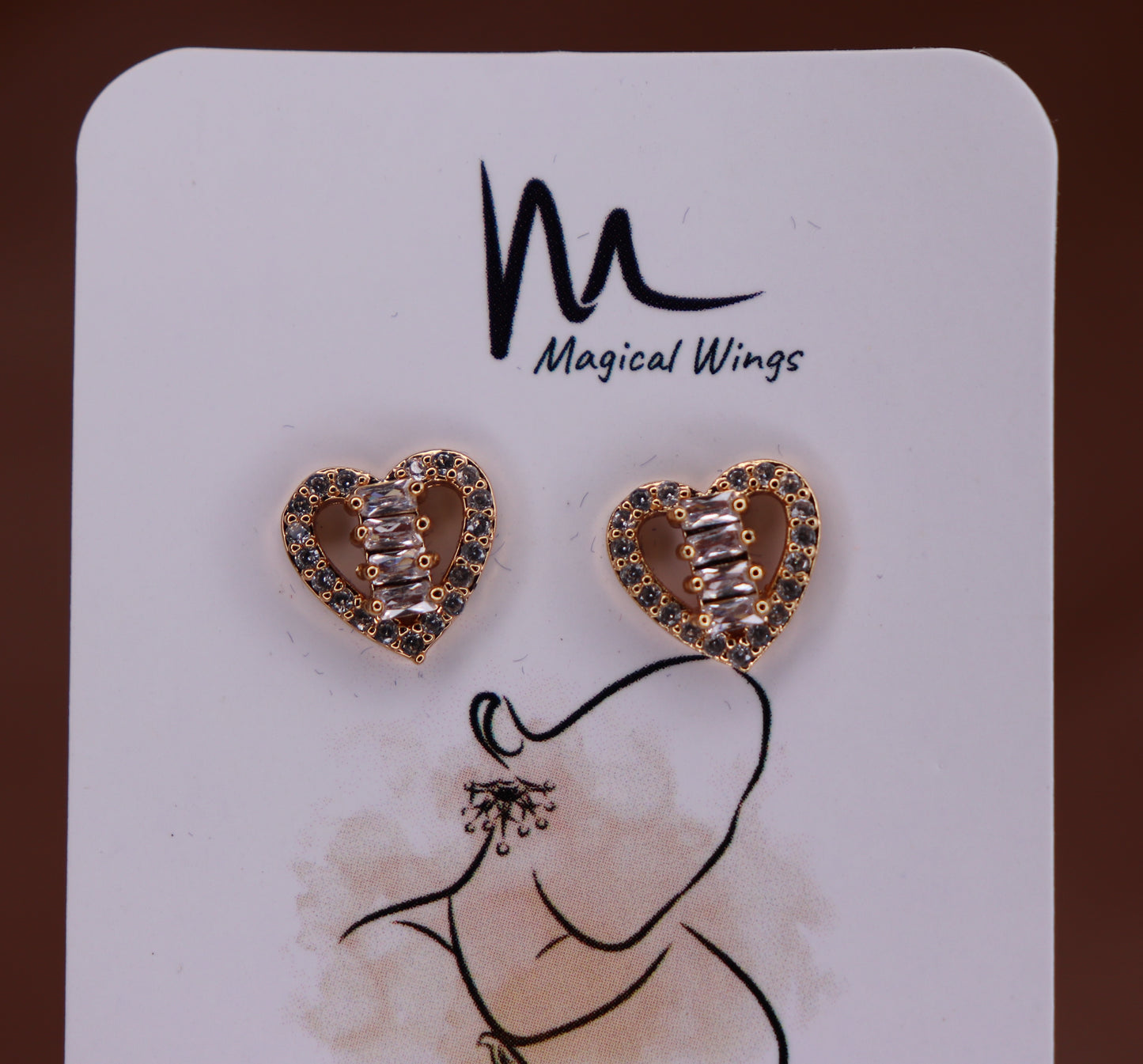 A pair of heart-shaped stud earrings with AD embellishments, displayed on a card with the brand name Magical Wings.