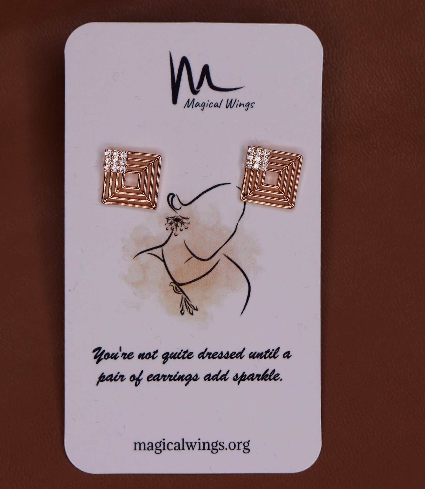 A rectangular card with a pair of stud earrings designed by Magical Wings. The earrings feature a bronze-colored hoop with white and rose gold accents.