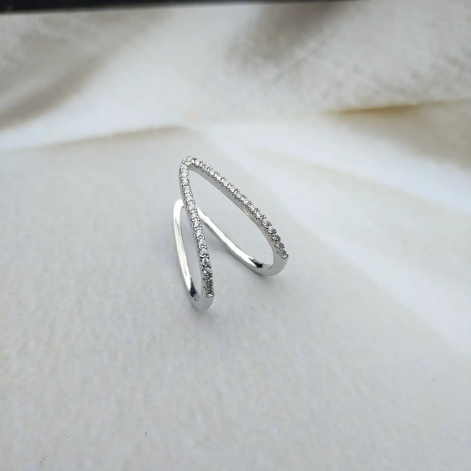 A 18kt white gold chevron ring with small diamonds set on the bands, displayed on a white fabric surface.