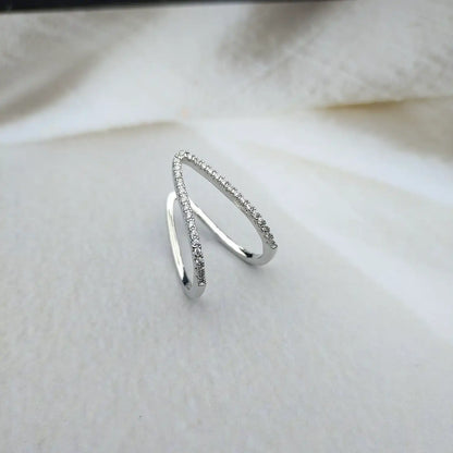 A 18kt white gold chevron ring with small diamonds set on the bands, displayed on a white fabric surface.