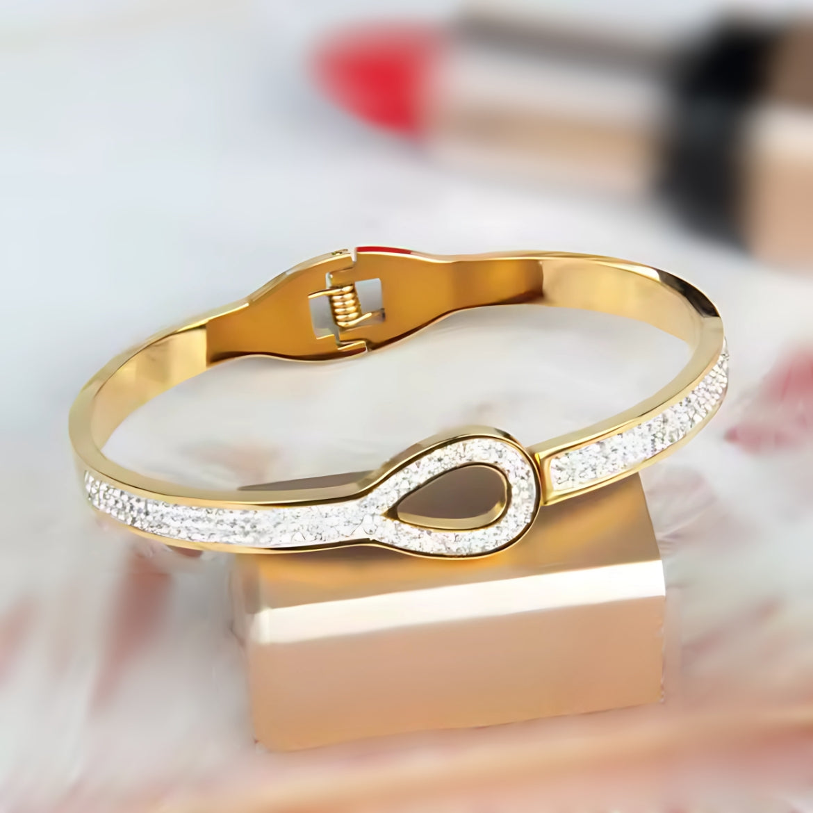 A gold-colored bangle bracelet with a link design and zirconia stones, displayed on a stand.