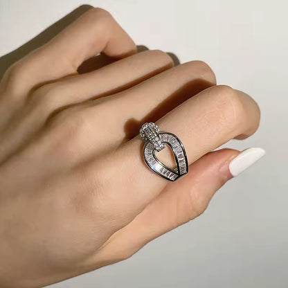 A hand showcasing a white crystal clear ring with a heart-shaped design and intricate details.