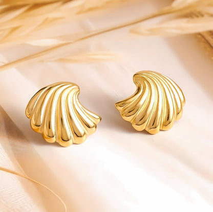 A pair of gold-colored shell-shaped stud earrings displayed on a beige fabric surface.