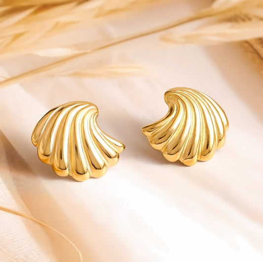 A pair of gold-colored shell-shaped stud earrings displayed on a beige fabric surface.