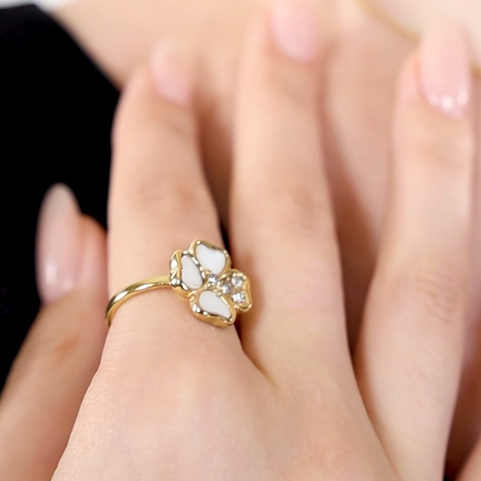 A 18k Gold Plated gold floral ring with a clear central gemstone and white accents on a person's finger.