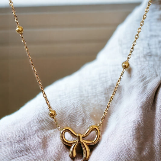 A gold bow ball chain pendant necklace displayed on a mannequin.