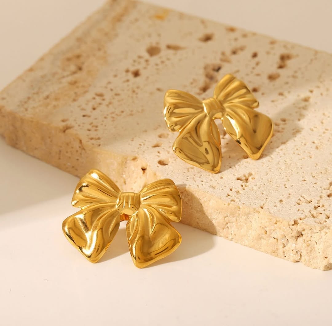 This image displays a pair of elegant 18kt gold earrings, shaped like bows. The earrings exhibit a glossy finish that enhances their sophisticated appeal.