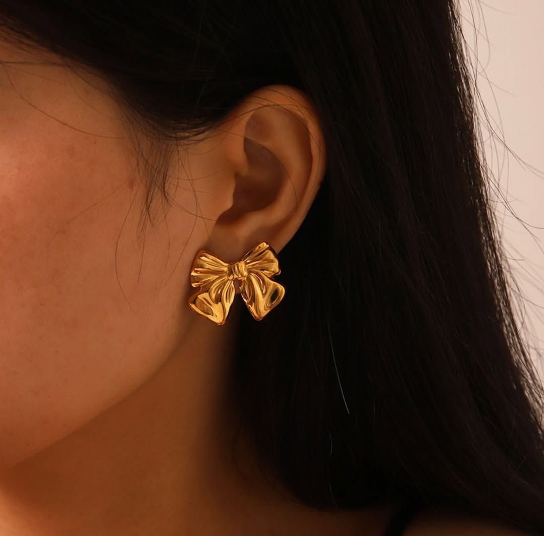 A close-up image of a person wearing a gold bow-shaped stud earring.