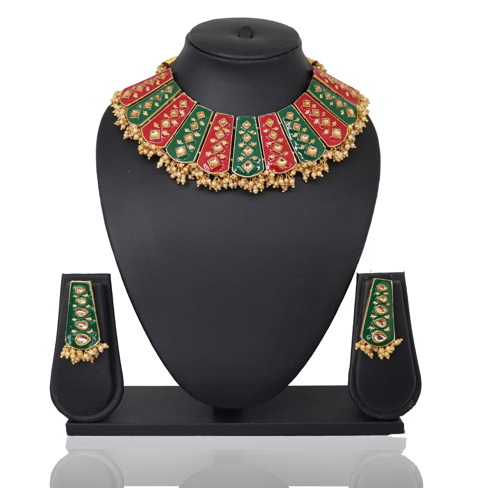A red-green meenakari kundan set displayed on a black mannequin, including a necklace, earrings, a mangtikka, and two bangles.
