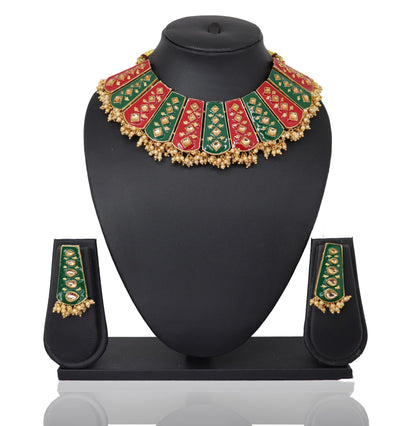 A red-green meenakari kundan set displayed on a black mannequin, including a necklace, earrings, a mangtikka, and two bangles.