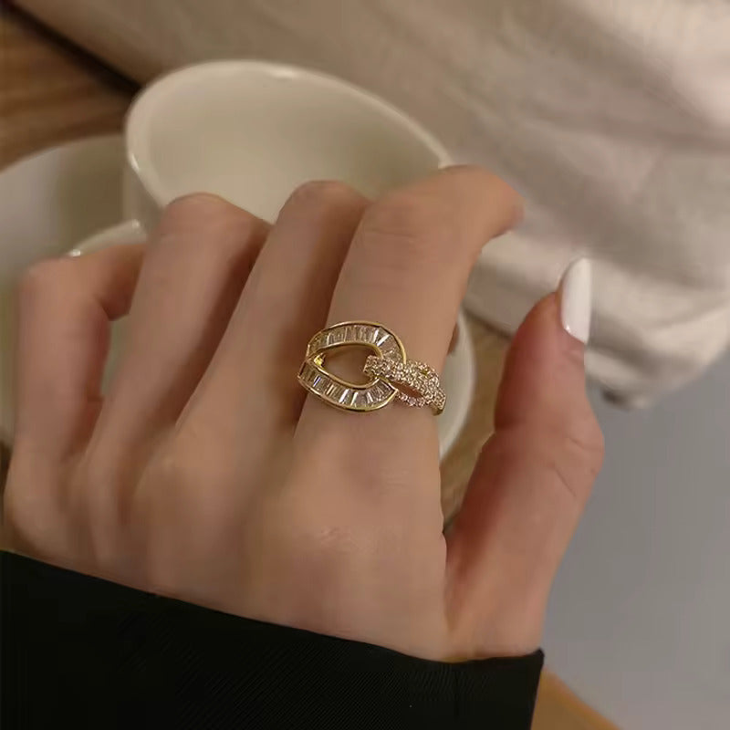 A gold-colored ring with clear crystals is displayed on a person's finger, which is resting on a white cup.