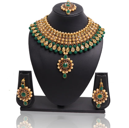 A set of jade and gold-colored jewelry including a necklace, earrings, and a maangtikka, displayed on a black stand.