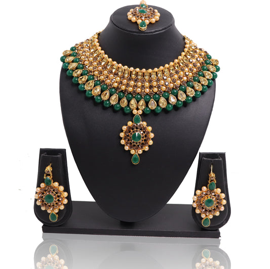 A set of jade and gold-colored jewelry including a necklace, earrings, and a maangtikka, displayed on a black stand.