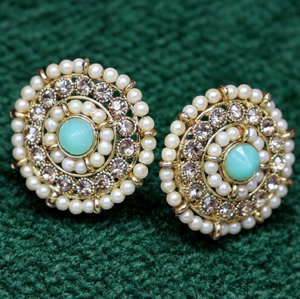A pair of jade kundan stud earrings with a gold-colored frame and green jade accents set on a green background.