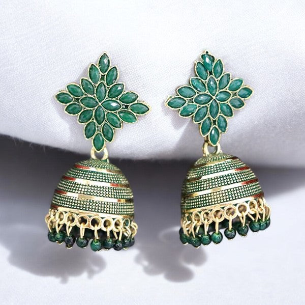A pair of dark green and gold-colored jhumka earrings displayed against a white fabric background.
