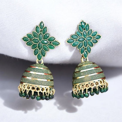 A pair of dark green and gold-colored jhumka earrings displayed against a white fabric background.