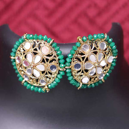 A pair of dark green kundan style stud earrings displayed against a red background.
