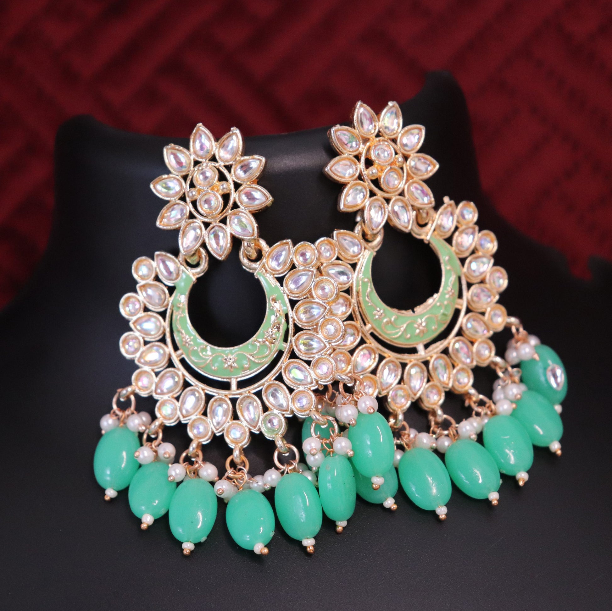 A pair of gold-toned chandbali earrings featuring green meenakari kundan style and drop-shaped beads.