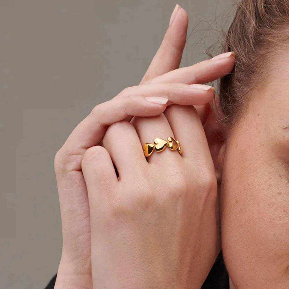 A close-up of a person's hand showcasing a gold ring with heart motifs on the finger.